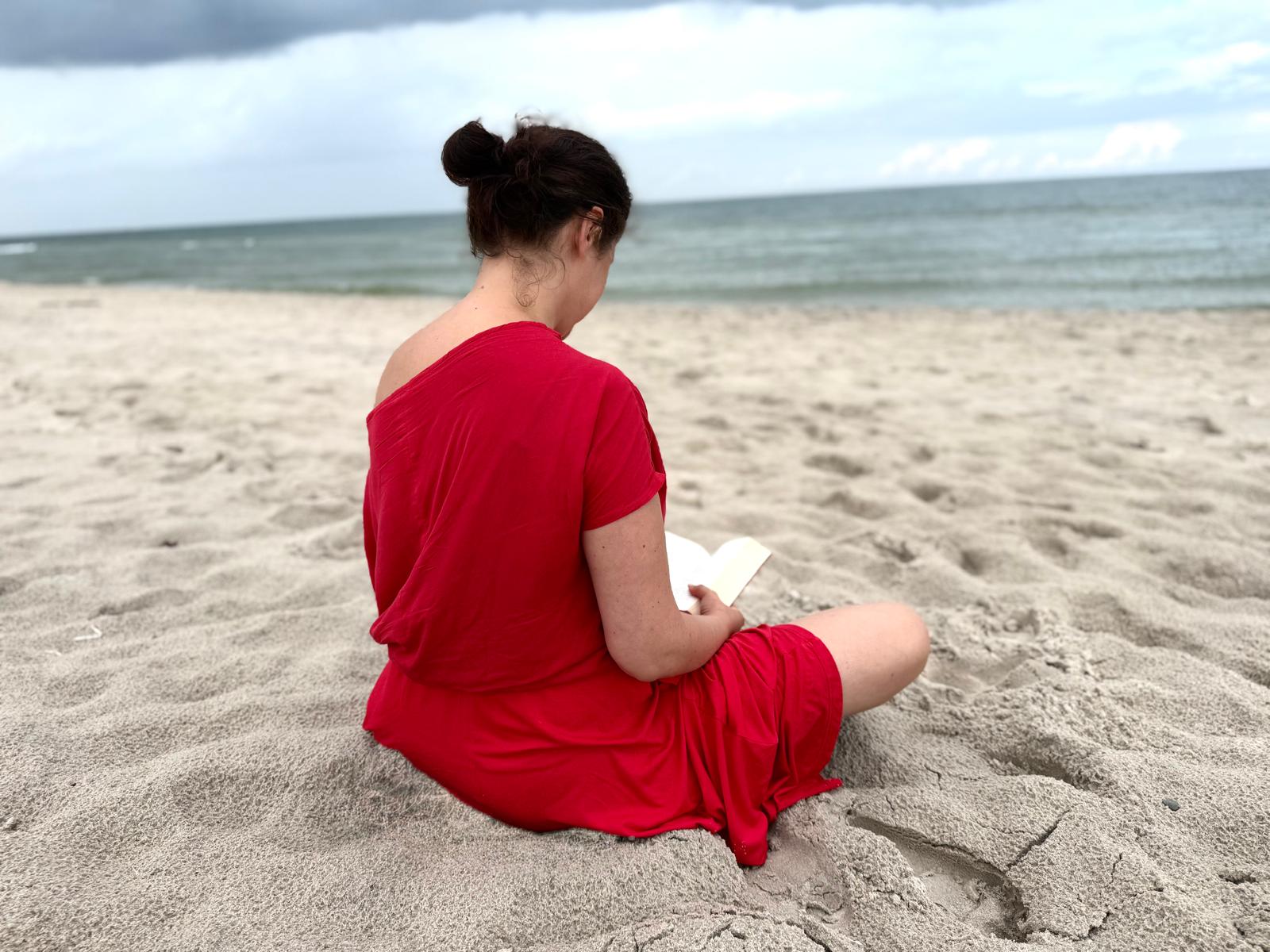 Karolina w czerwonej sukience czytająca książkę na plaży nad morzem